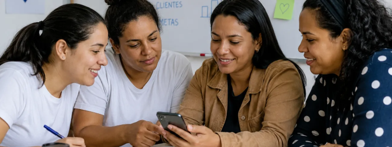 Mulheres refugiadas participando de curso de empreendedorismo com uso de celular e atividades colaborativas.