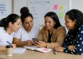 Mulheres refugiadas participando de curso de empreendedorismo com uso de celular e atividades colaborativas.