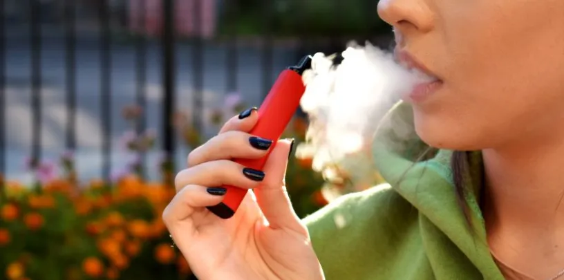 Pessoa utilizando cigarro eletrônico, liberando vapor em ambiente externo