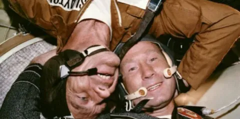 Astronautas americanos e soviéticos trabalhando juntos durante o Projeto Apollo–Soyuz, simbolizando colaboração apesar das rivalidades geopolíticas.