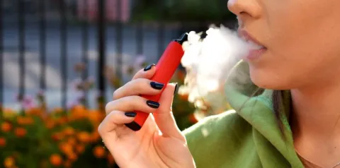 Pessoa utilizando cigarro eletrônico, liberando vapor em ambiente externo