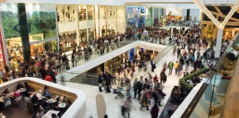 Movimento intenso de pessoas em shopping center com lojas abertas em vários andares.