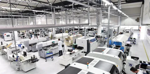 Linha de produção industrial com máquinas automatizadas e técnicos trabalhando em fábrica moderna de eletrônicos