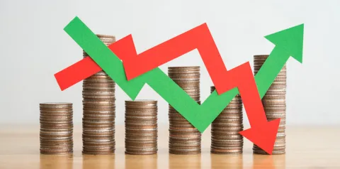 Pilhas de moedas organizadas em diferentes alturas com setas verdes e vermelhas sobrepostas, indicando alta e queda em indicadores financeiros